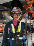 Person wearing safety gear including a helmet and harness, standing in an industrial setting.