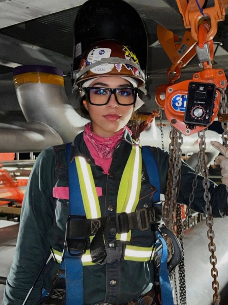 Person wearing safety gear including a helmet and harness, standing in an industrial setting.