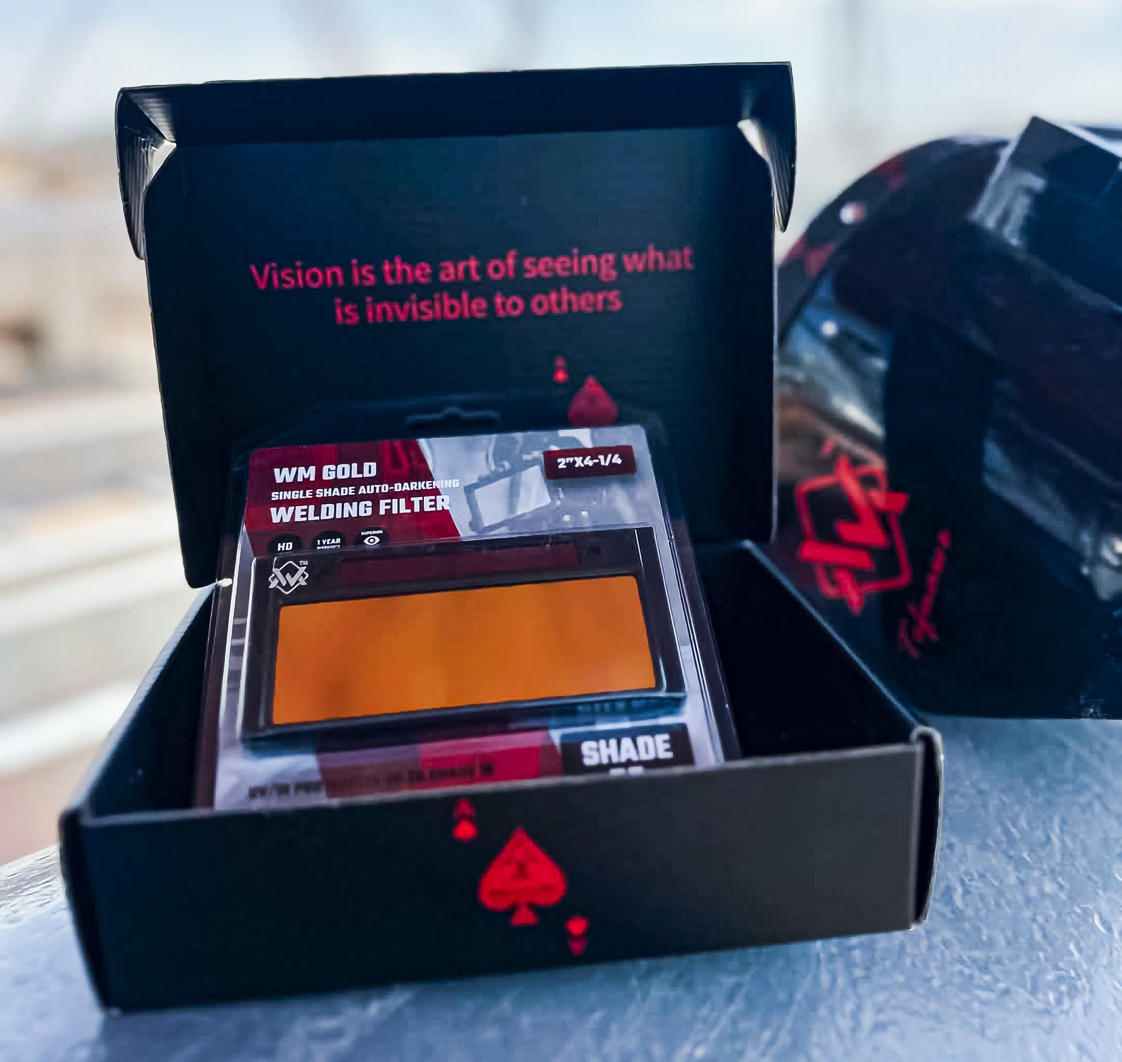 Black box with a welding filter inside, featuring text and a red spade symbol.