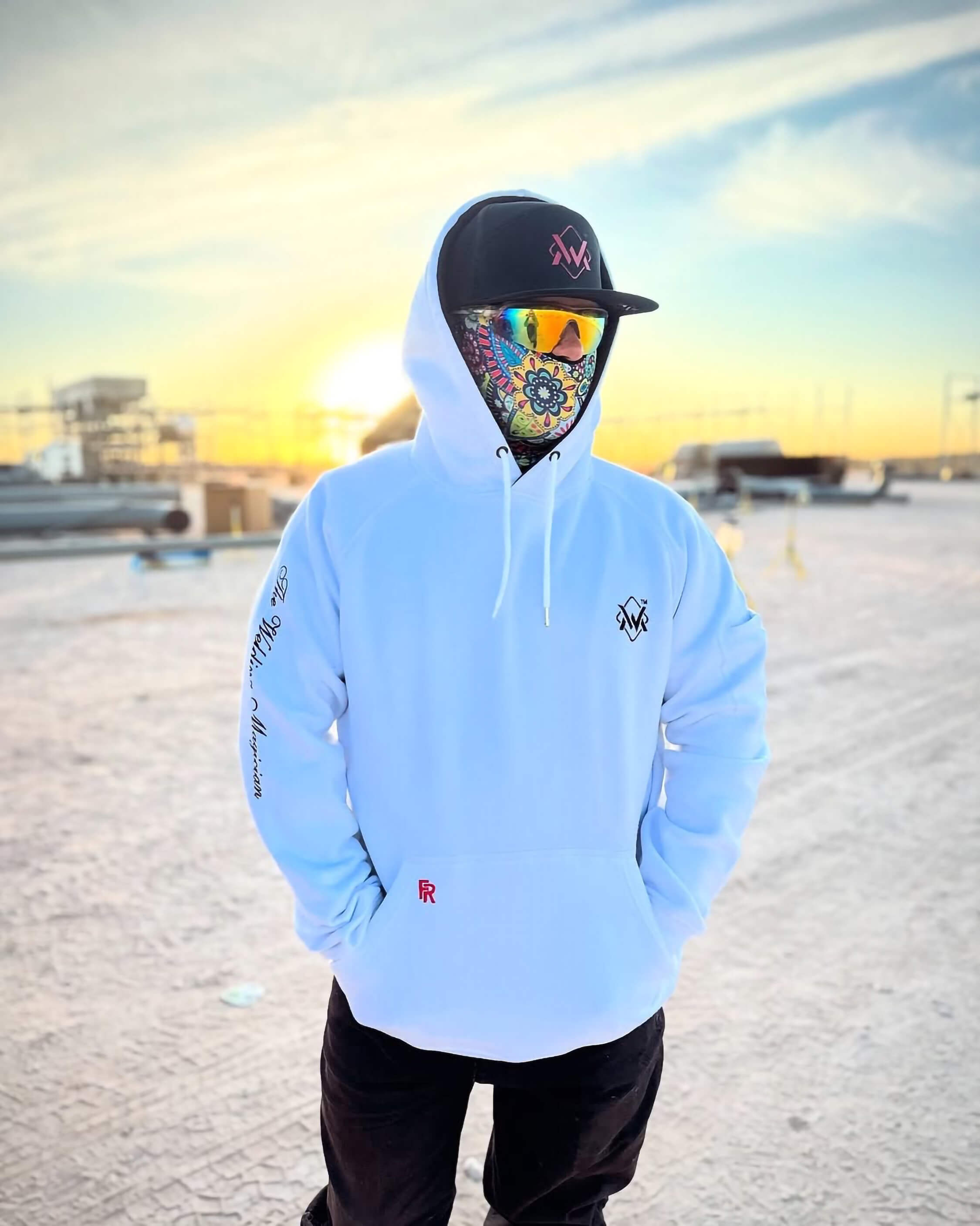 Person wearing a white hoodie and colorful mask with a sunset in the background