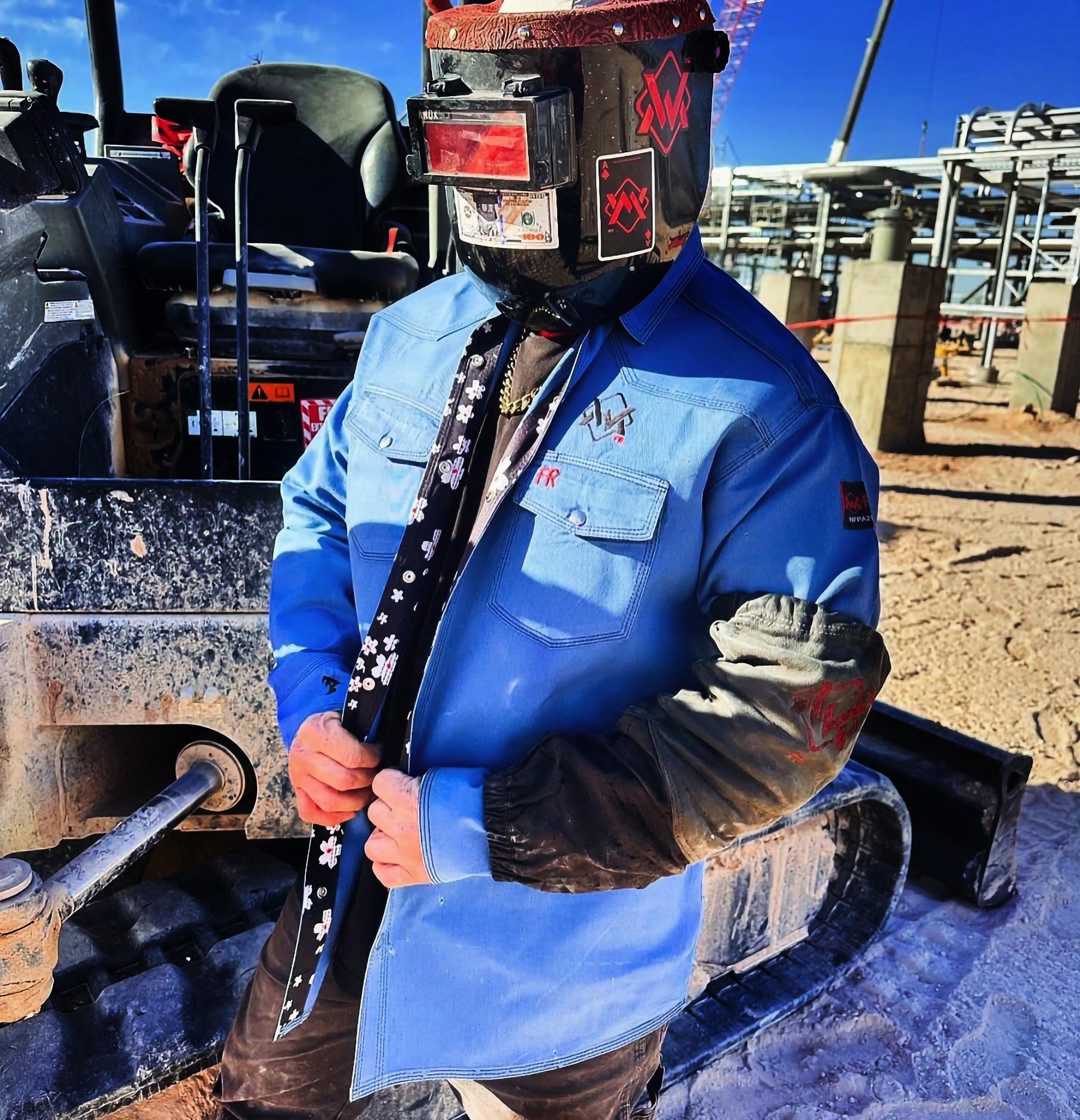 Person wearing a blue shirt and welding helmet in front of a tractor