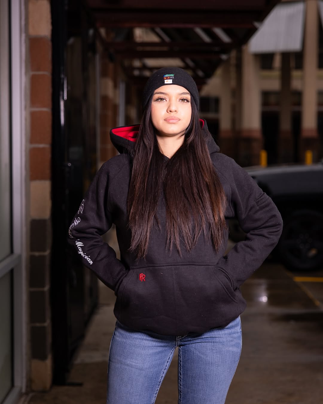 Woman wearing a black hoodie with red accents and a beanie, standing outdoors.