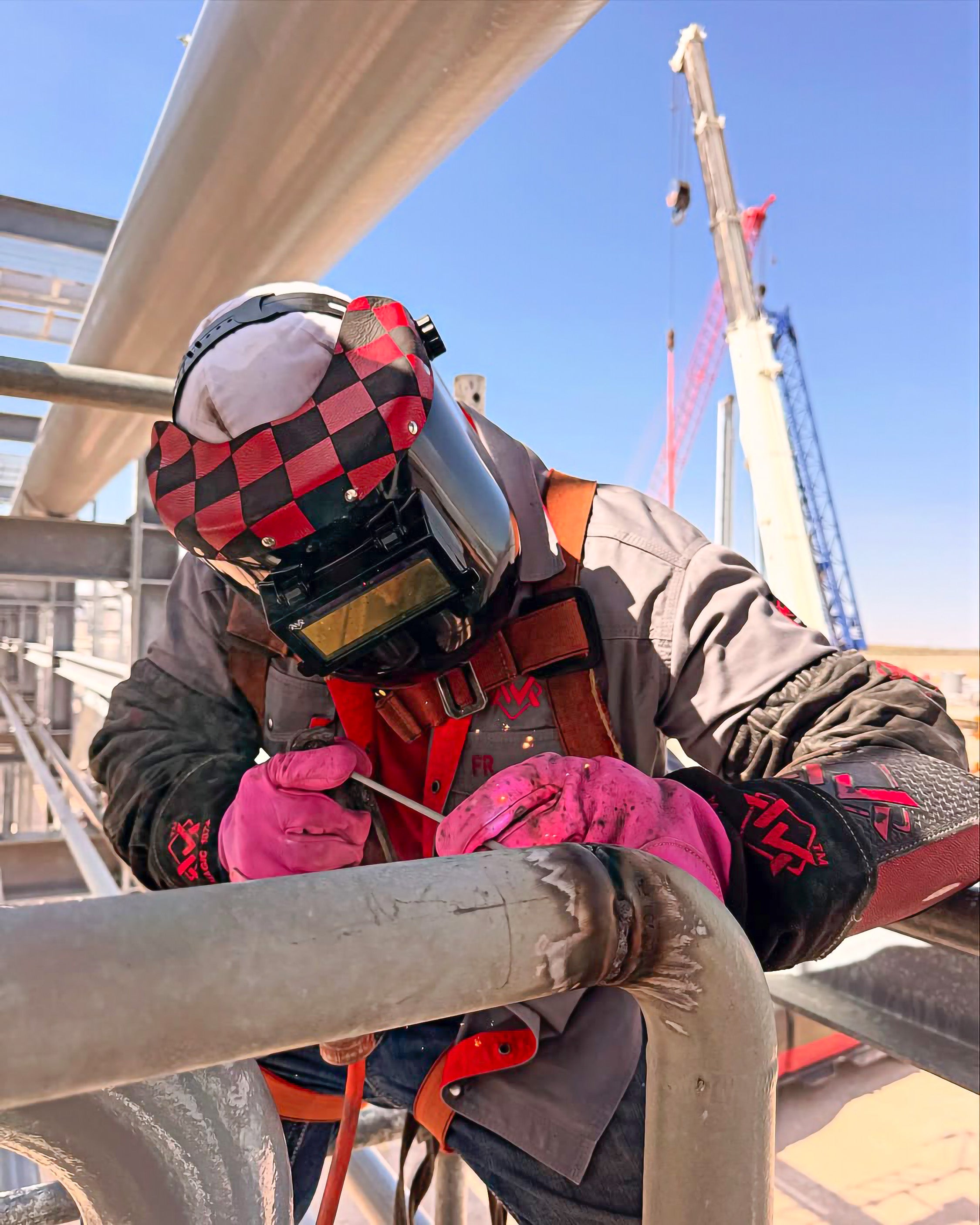 Person wearing protective gear welding metal pipes on a construction site.