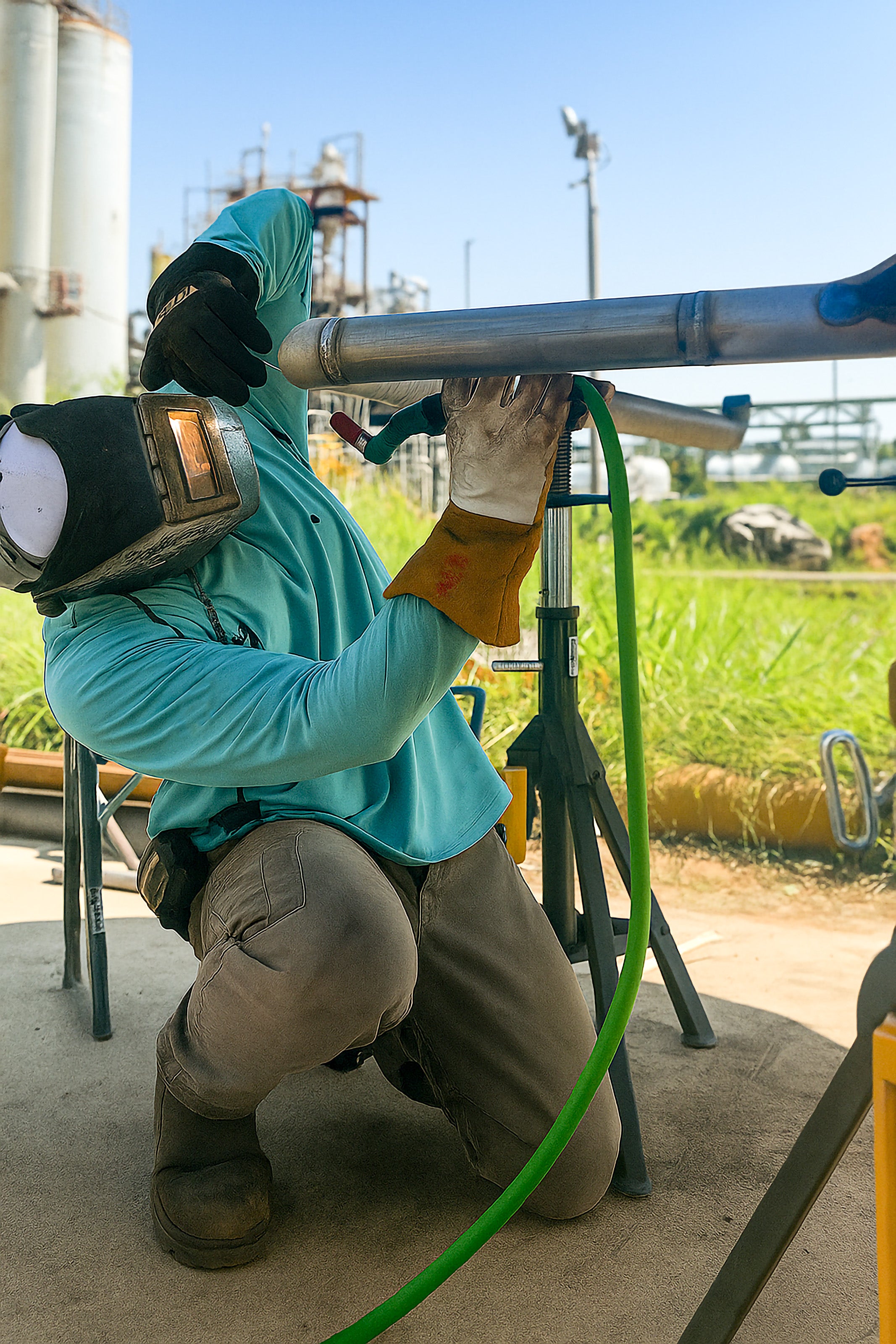 Person welding in an industrial setting with equipment and tanks in the background