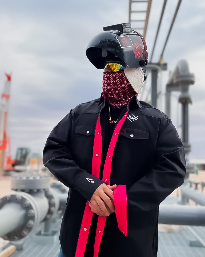 Person wearing a black helmet with a visor, black jacket, and red accents in an industrial setting.