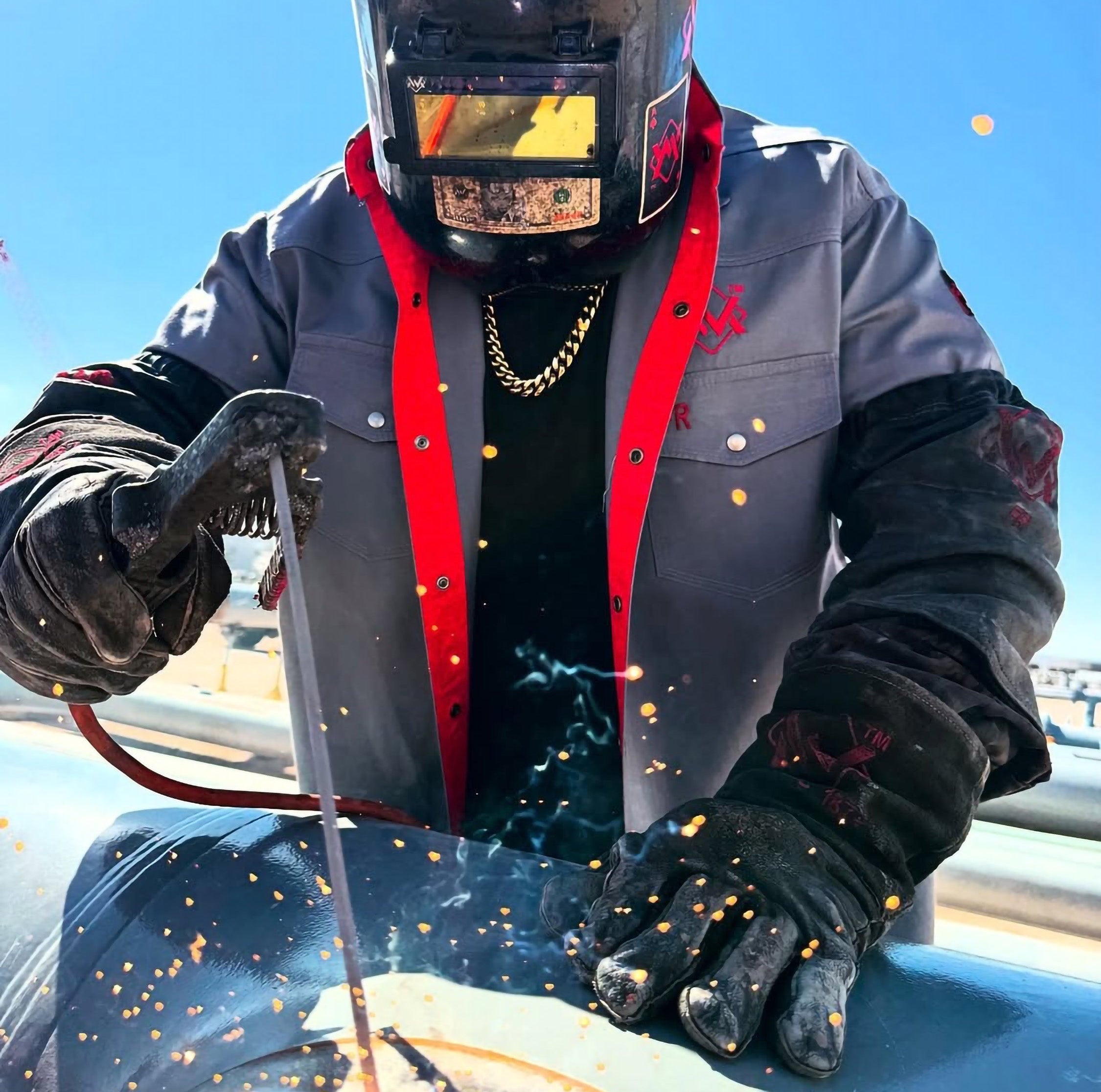 Person welding with protective gear against a blue sky
