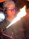 Person wearing protective gear with a flame in an industrial setting