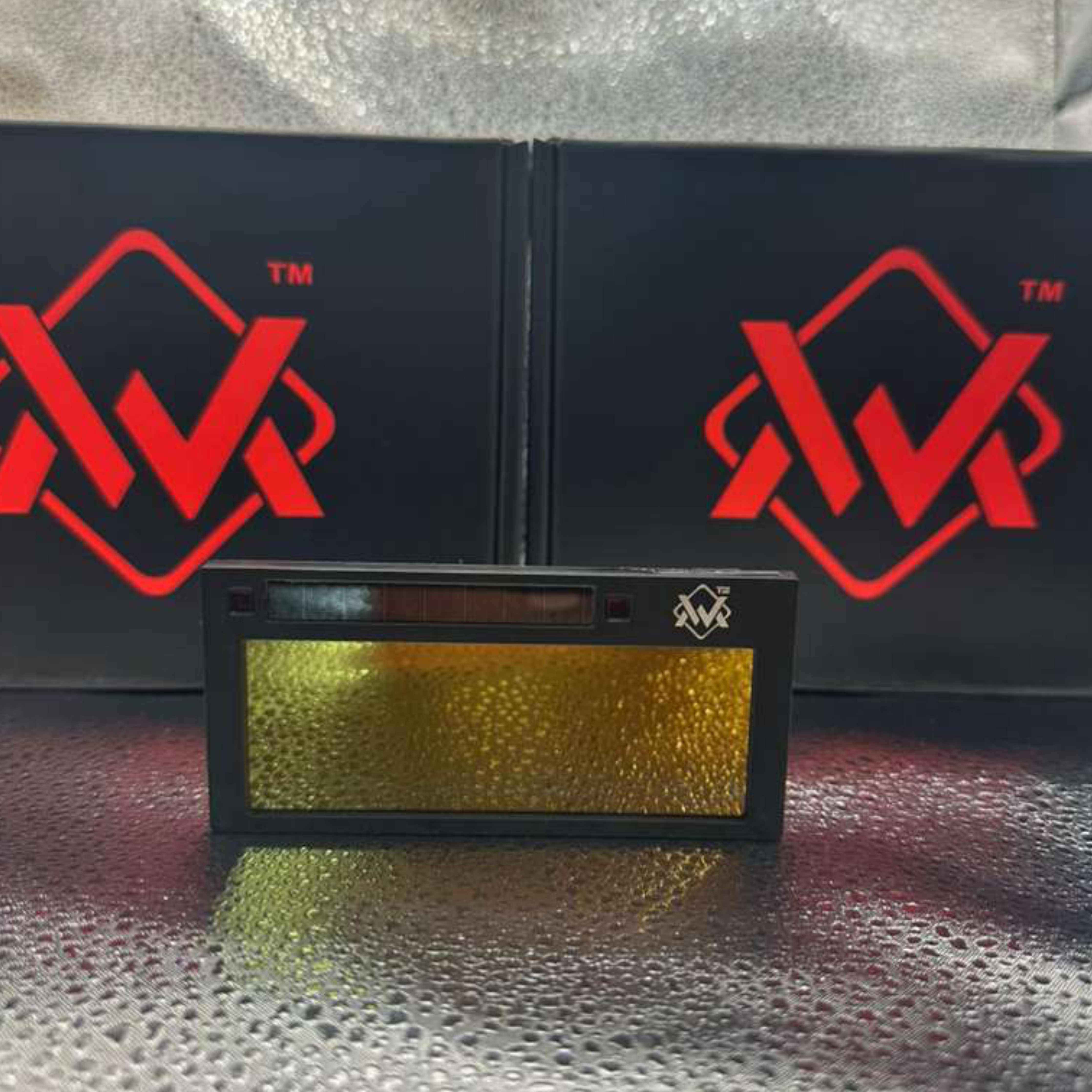 WM GOLD Digital Welding Lens true color auto-darkening replacement filter with gold lens surface displayed in front of The Welding Magician logo boxes