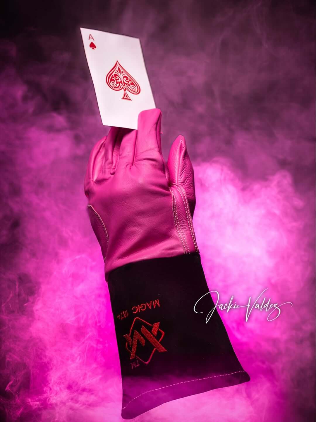 Hand wearing a pink glove holding an Ace of Spades card against a pink smoke background