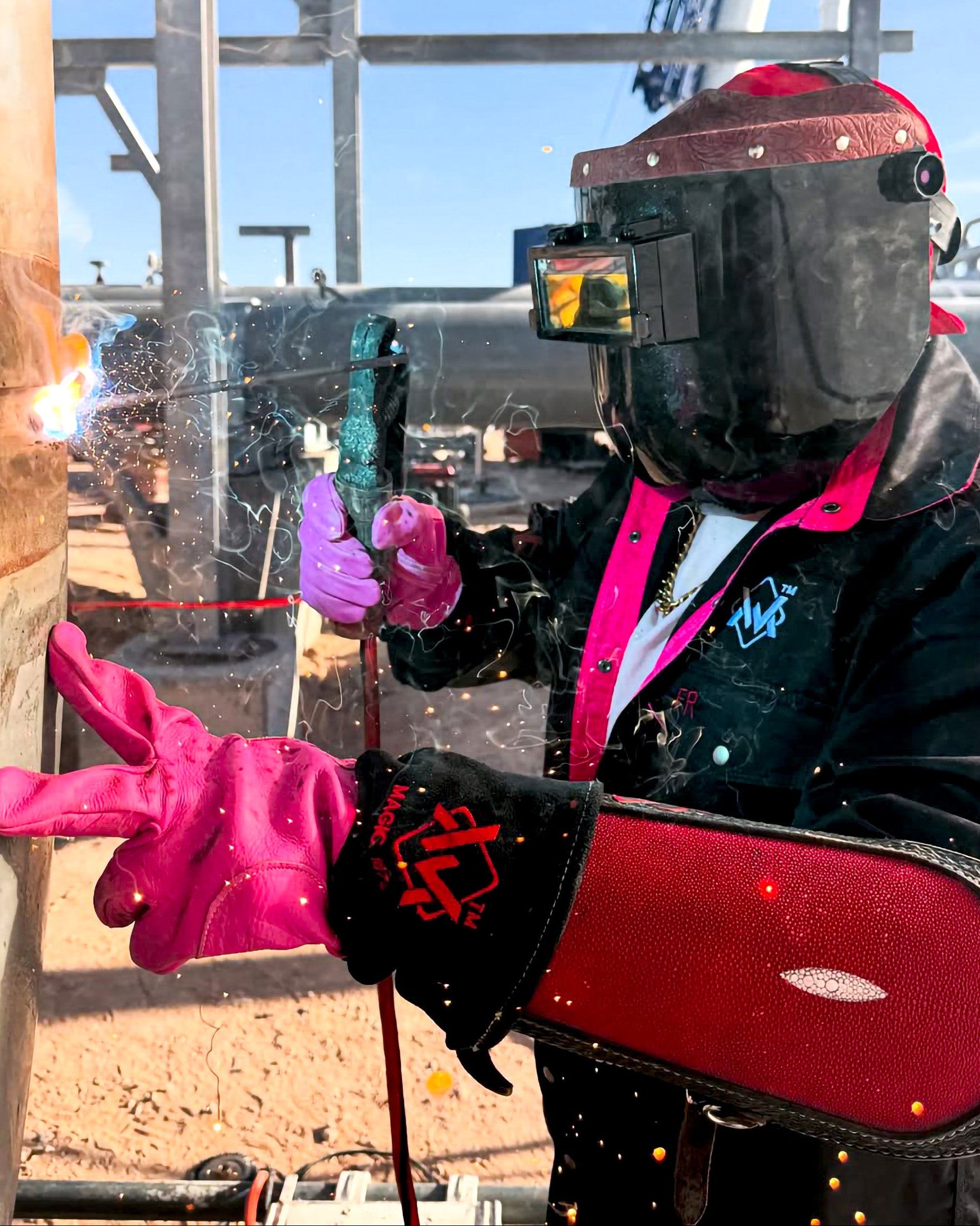 Person wearing a welding helmet and gloves holding a welding tool outdoors.