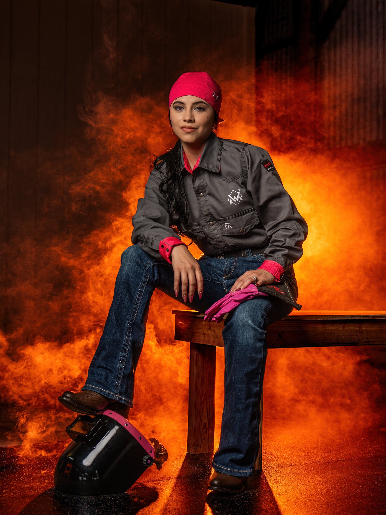 Person wearing a gray jacket with a logo, sitting on a stool against an orange background