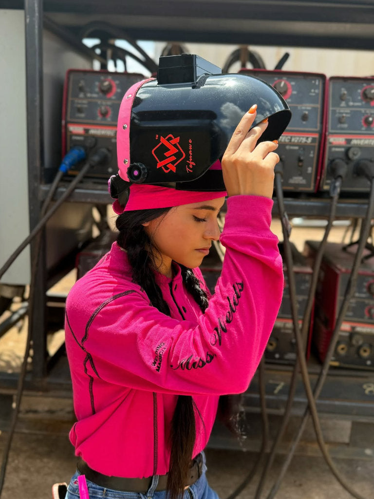 Person wearing a pink jacket and black helmet with a pink visor in an industrial setting.
