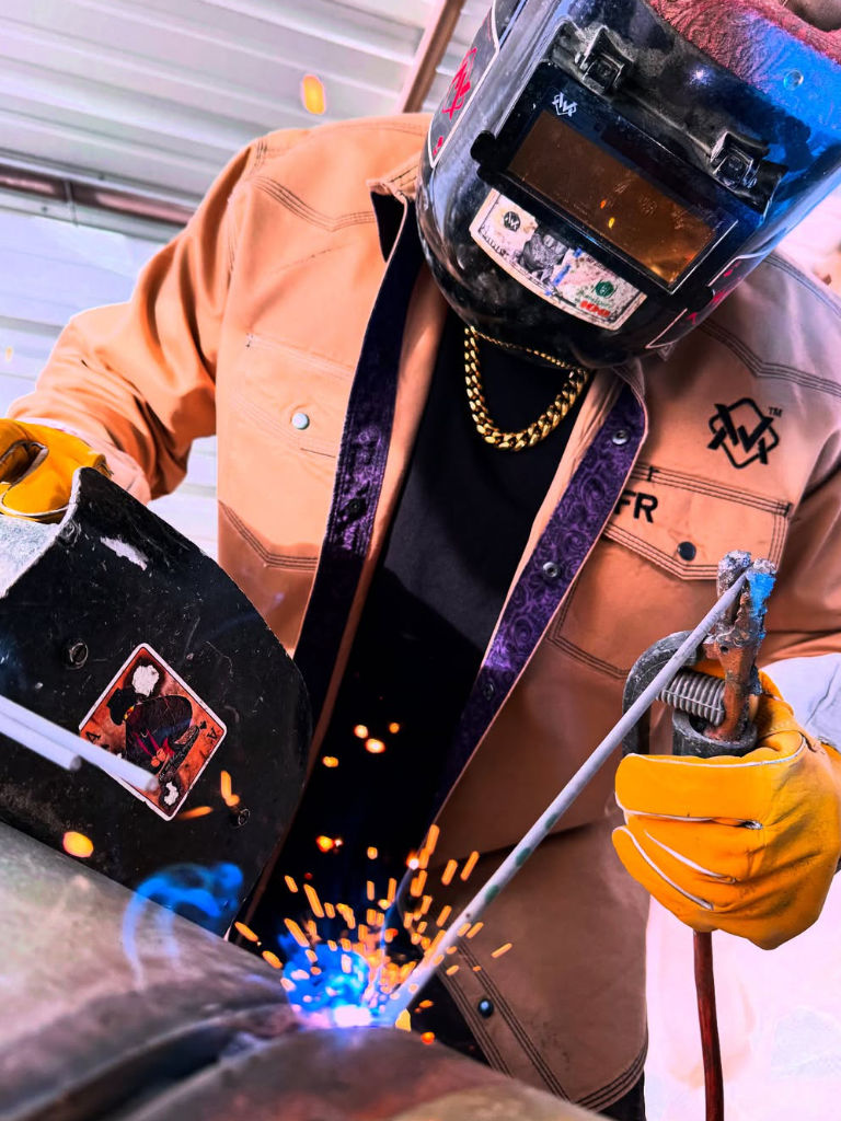 Person welding with sparks flying, wearing protective gear including a helmet and gloves.