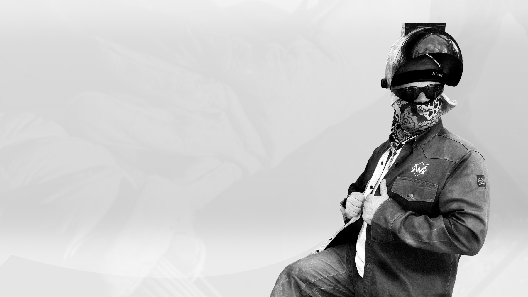 Welder wearing a flame-resistant welding shirt, helmet, sunglasses, and bandana, posing confidently in protective gear.