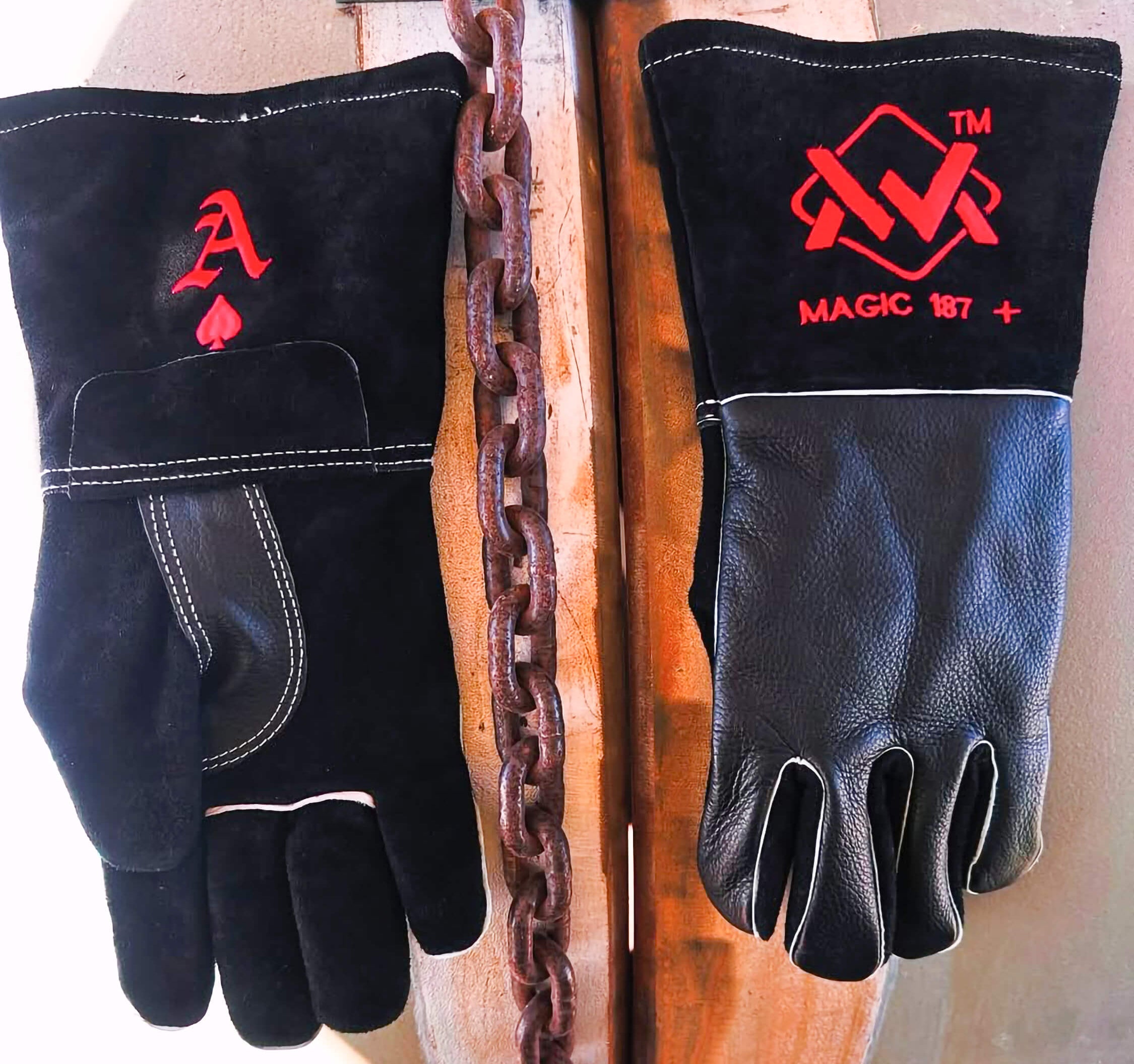 Pair of black leather gloves with red logos on a wooden surface with a chain.