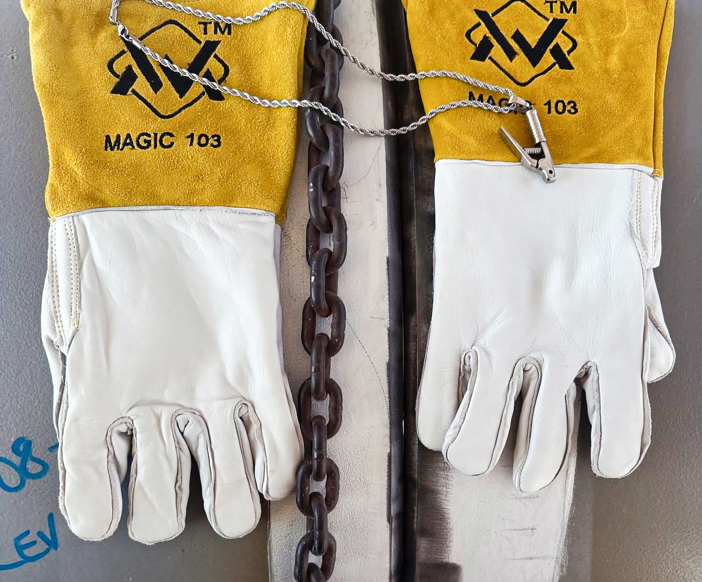 Pair of white gloves with yellow cuffs featuring a logo and text, hanging on a chain against a gray background.