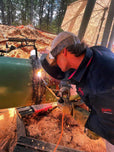 Person welding a pipe outdoors with construction equipment in the background