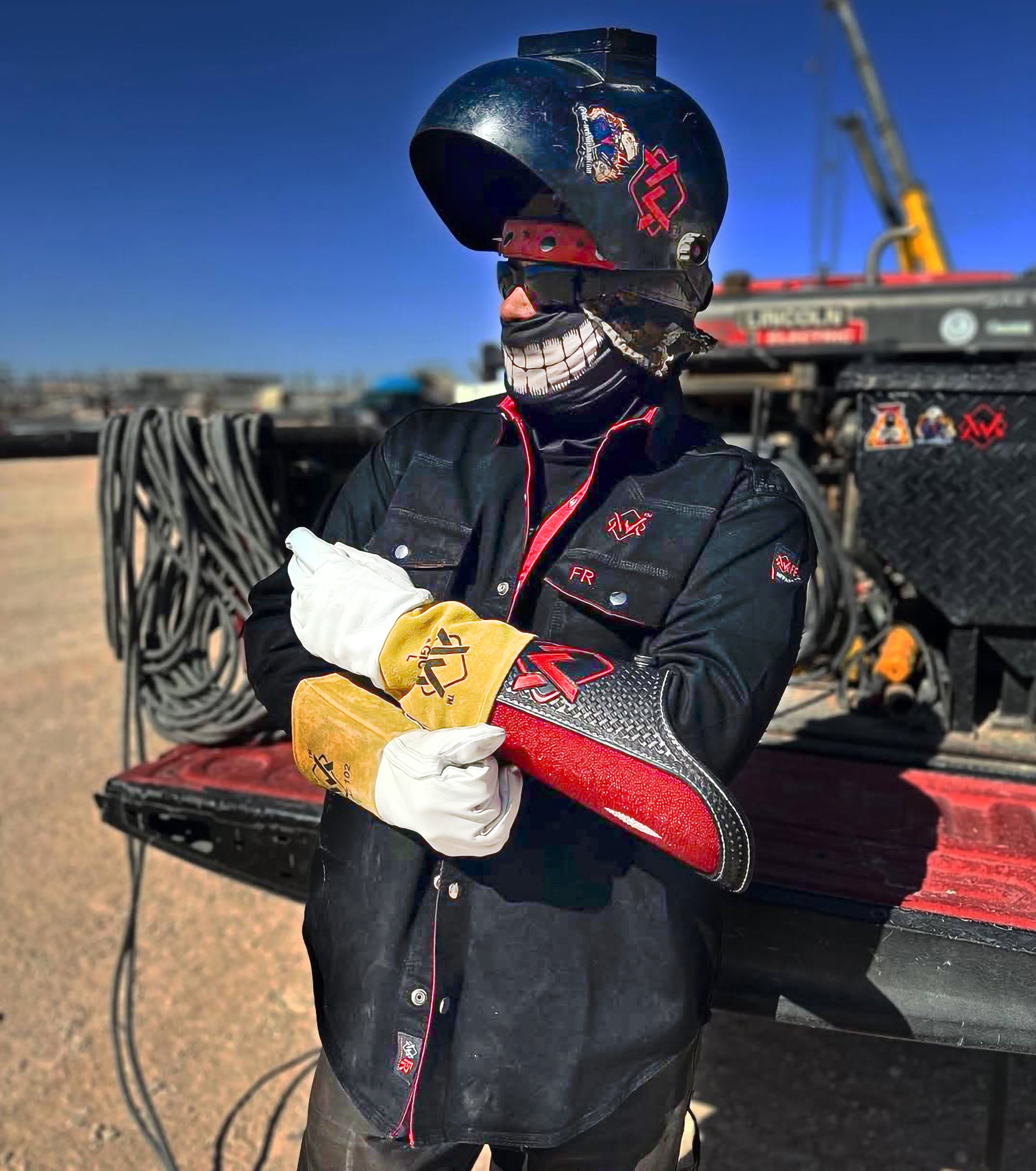 Person wearing a black helmet and gloves holding a yellow and red object, standing on a truck bed with a clear sky.