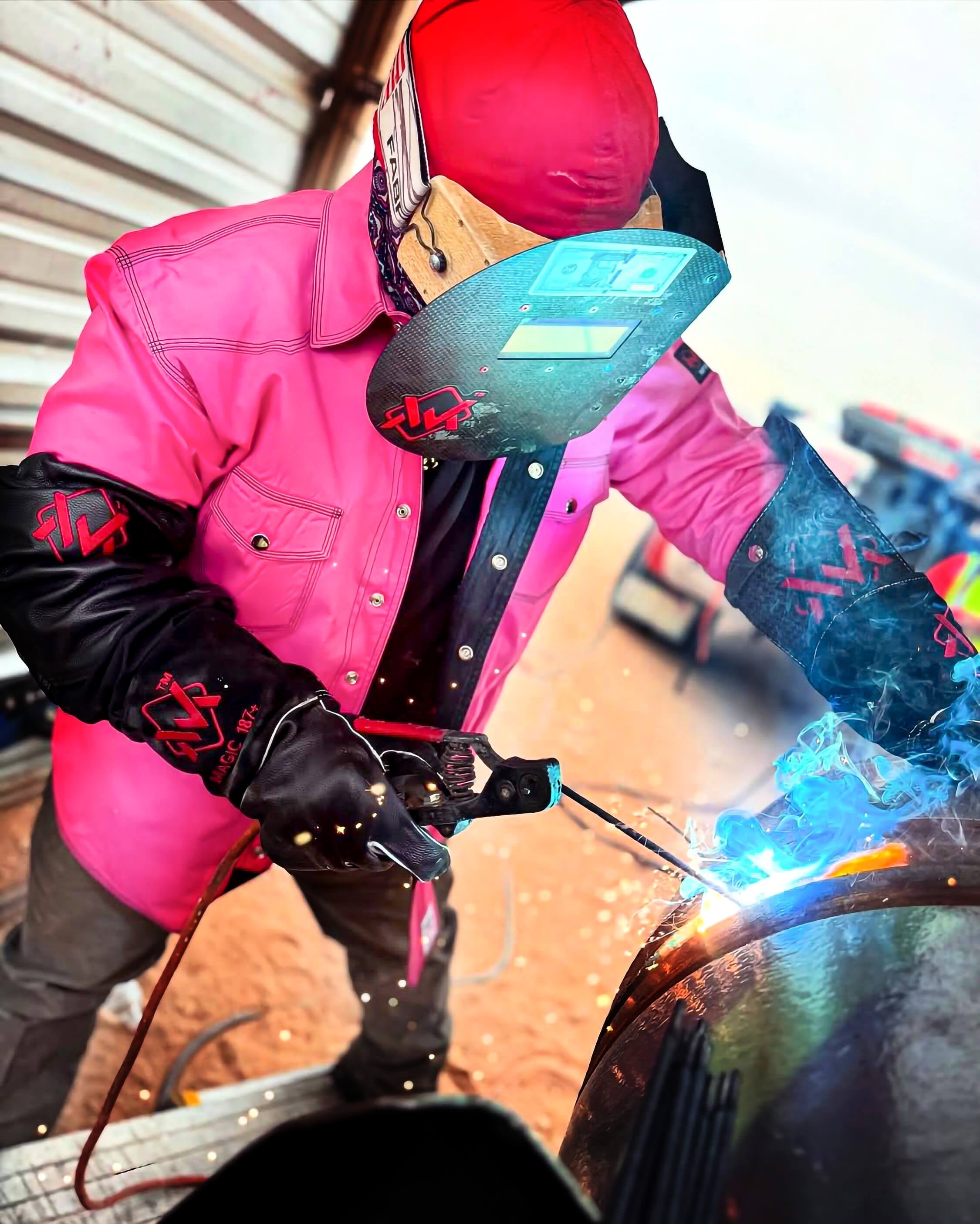 Person welding wearing a pink jacket and protective gear with a blurred background