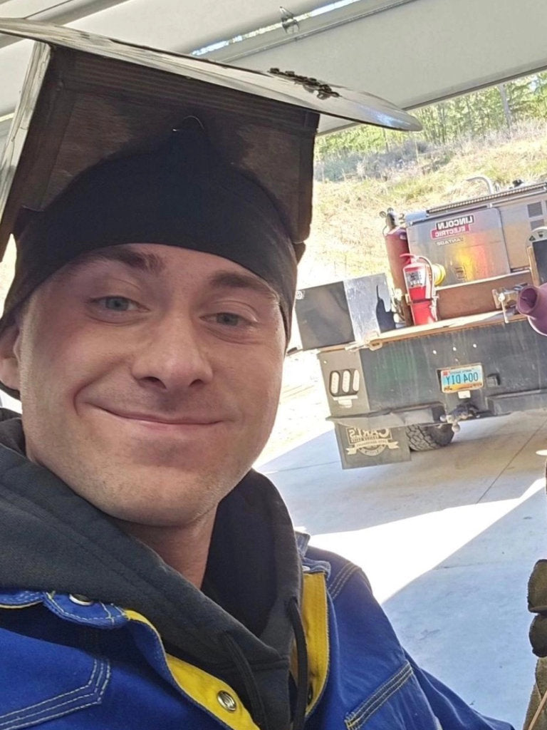 Man wearing a black beanie and blue jacket with a truck in the background