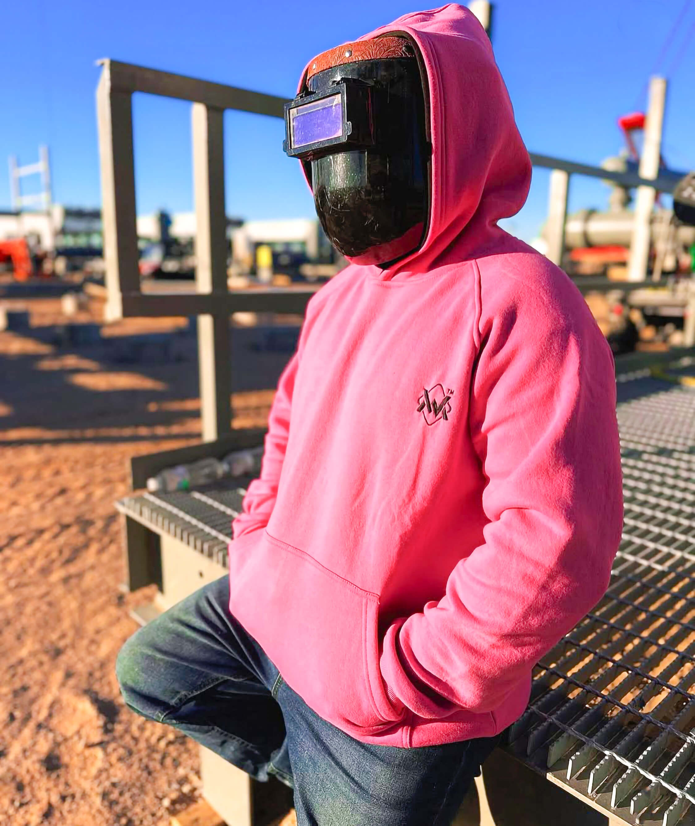 Person wearing a pink hoodie and welding mask outdoors