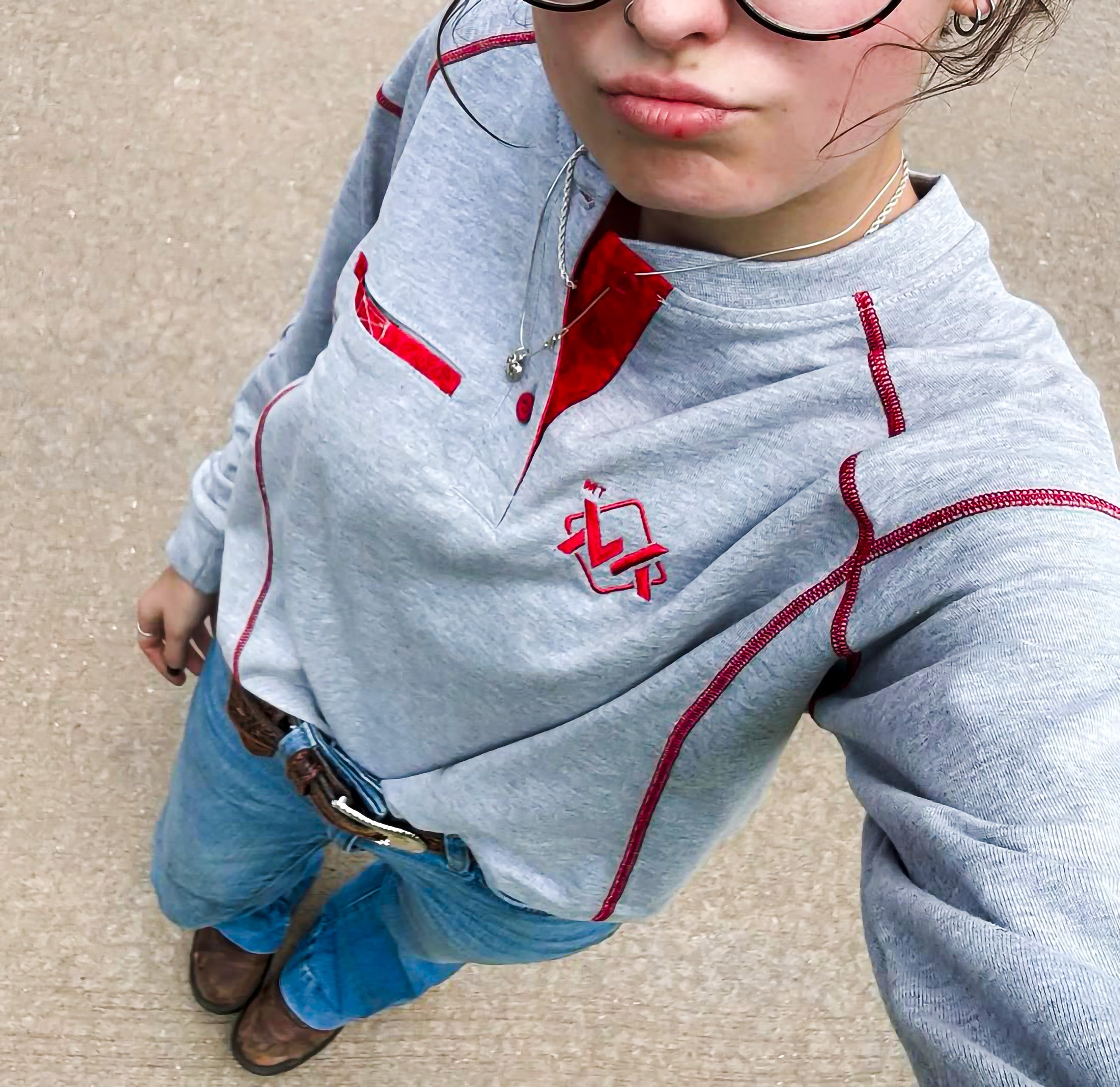 Person wearing a gray hoodie with red accents and a logo, standing on a beige surface.